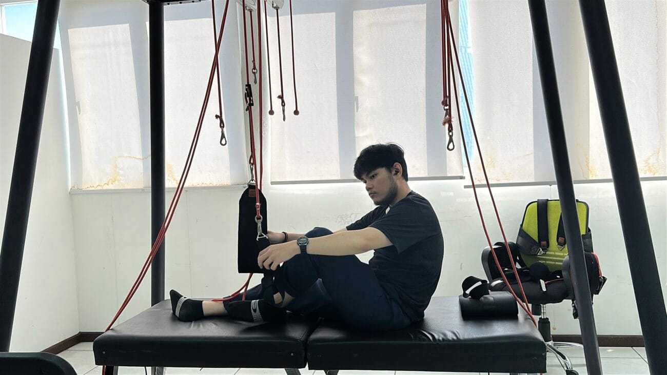 Seorang pasien melakukan latihan sling therapy di atas meja terapi dengan bantuan tali untuk rehabilitasi fisik.