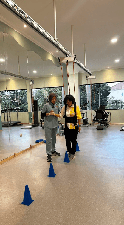 Pasien latihan berjalan dengan sling therapy dibantu terapis melewati rintangan